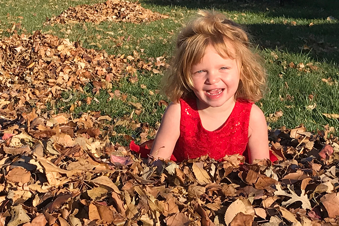 little girl sitting in pile of leaves